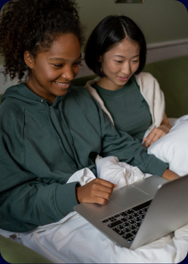 african and chinese women sitting on bed and looking at notebook considering to sign up for crypto Individual Learning classes: Crypto Fundamentals Mastery and Crypto Investment Accelerator